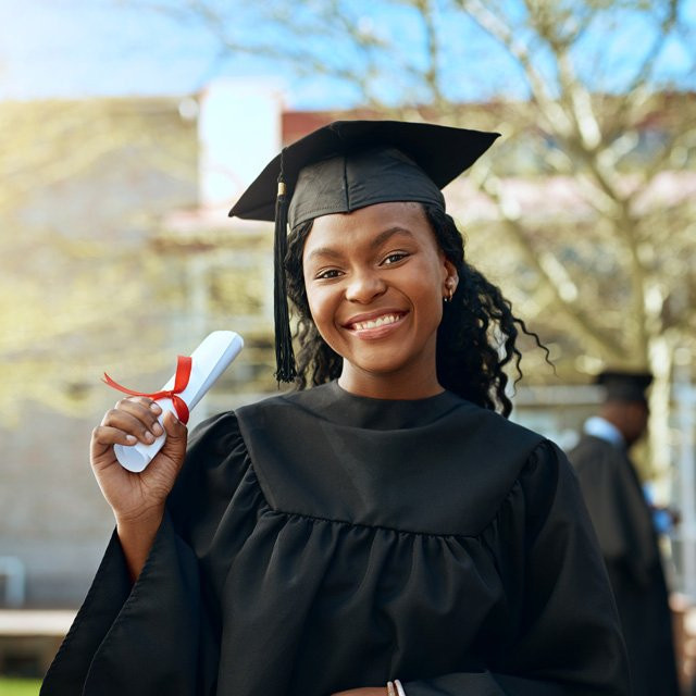 A recent graduate wearing her cap and gown, holding her diploma.
